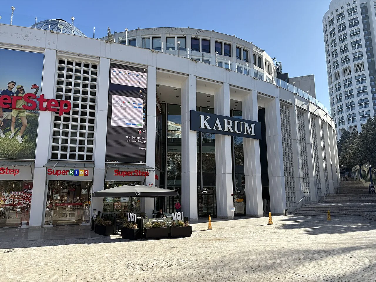 Karum alışveriş merkezinin KARUM yazılı ana girişi, beyaz sütunlu cephesi ve önündeki açık alan.