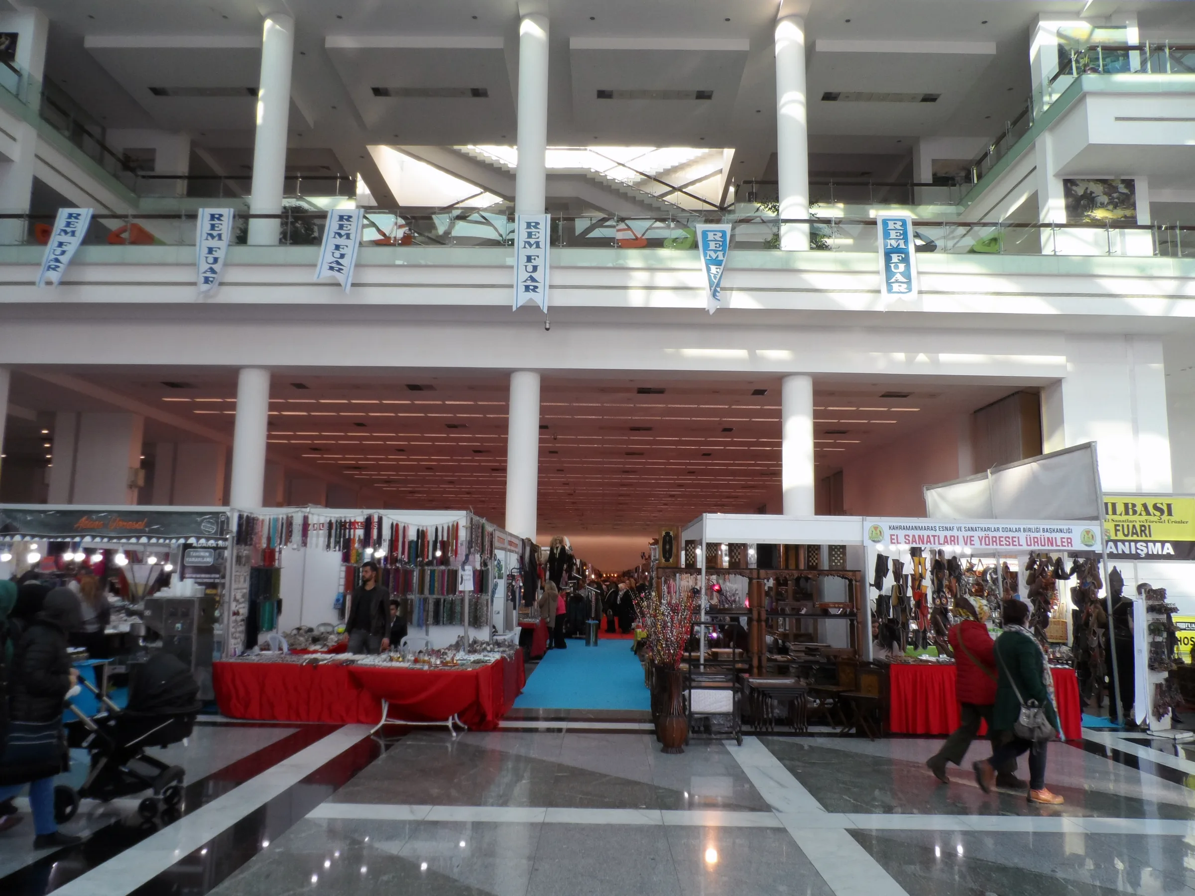 Craft-fair stalls in ATO Congresium's bright interior, with white columns, a tiled floor and an upper gallery