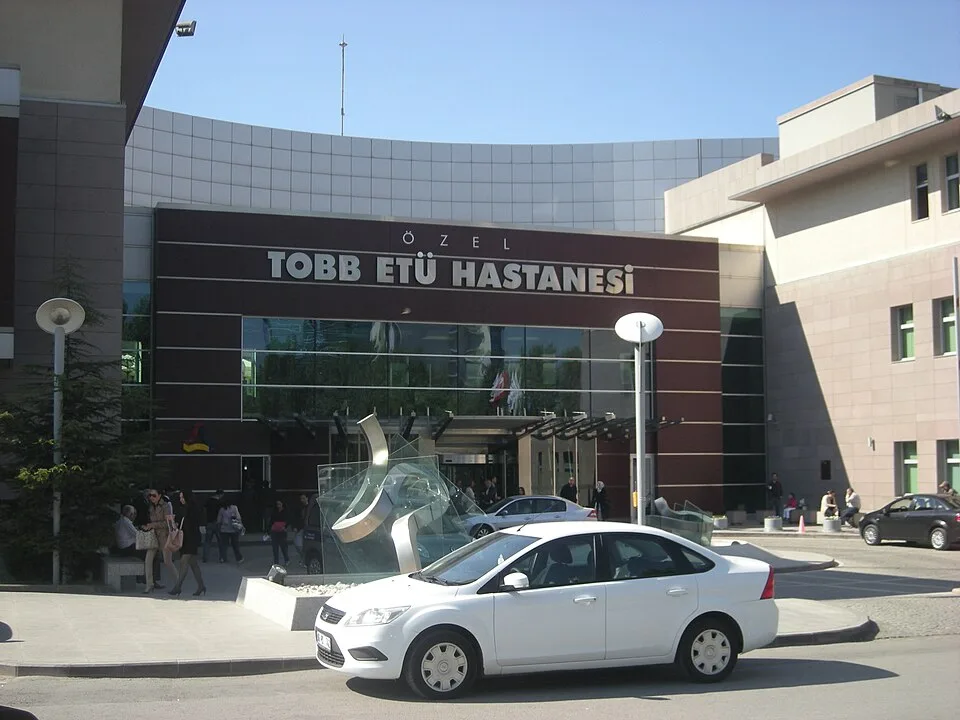 TOBB ETÜ Hastanesi'nin tabelalı cam giriş cephesi ve önündeki araçlar
