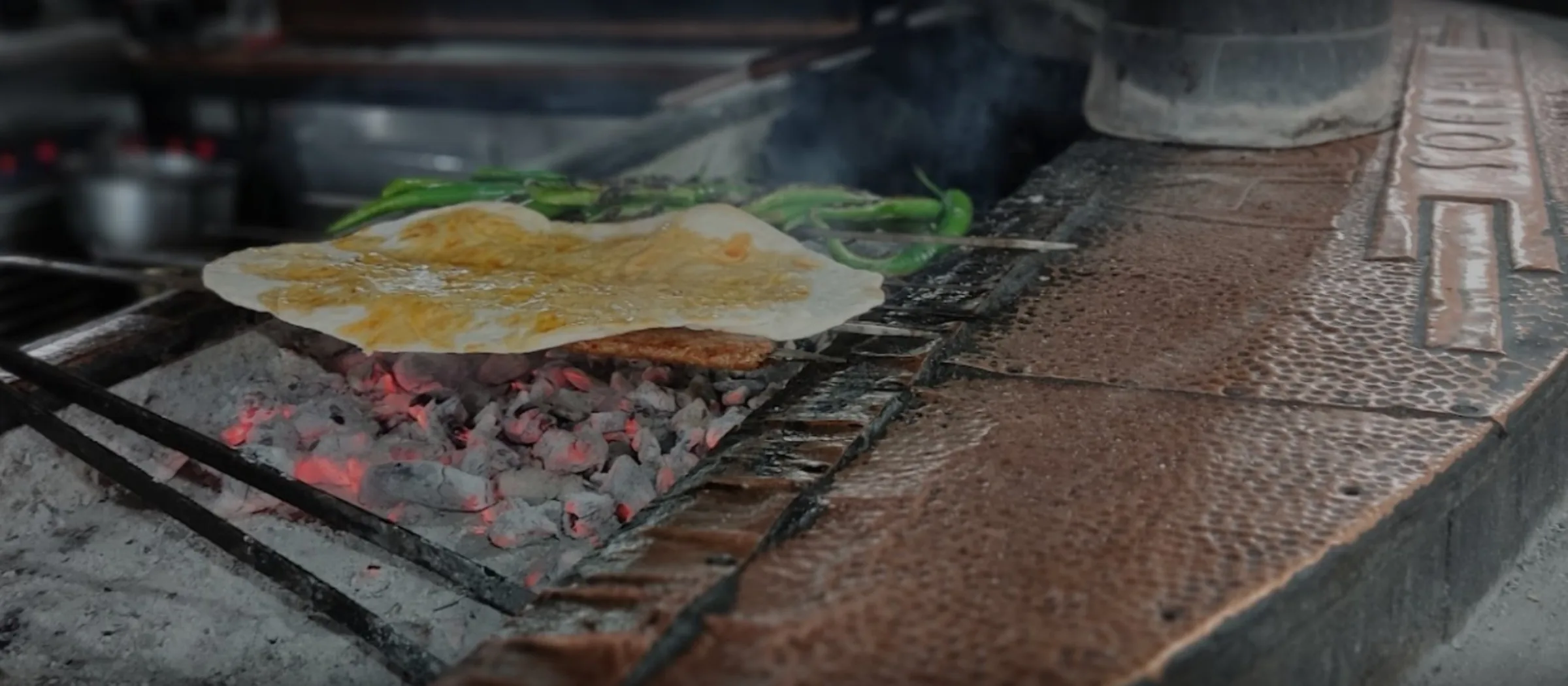 Long open charcoal grill with flatbread warming over the coals