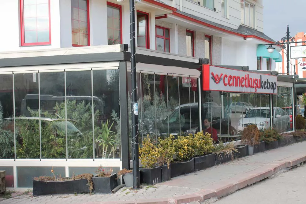 Glass-fronted entrance of Cennetkuşu Kebap with its red sign and potted plants