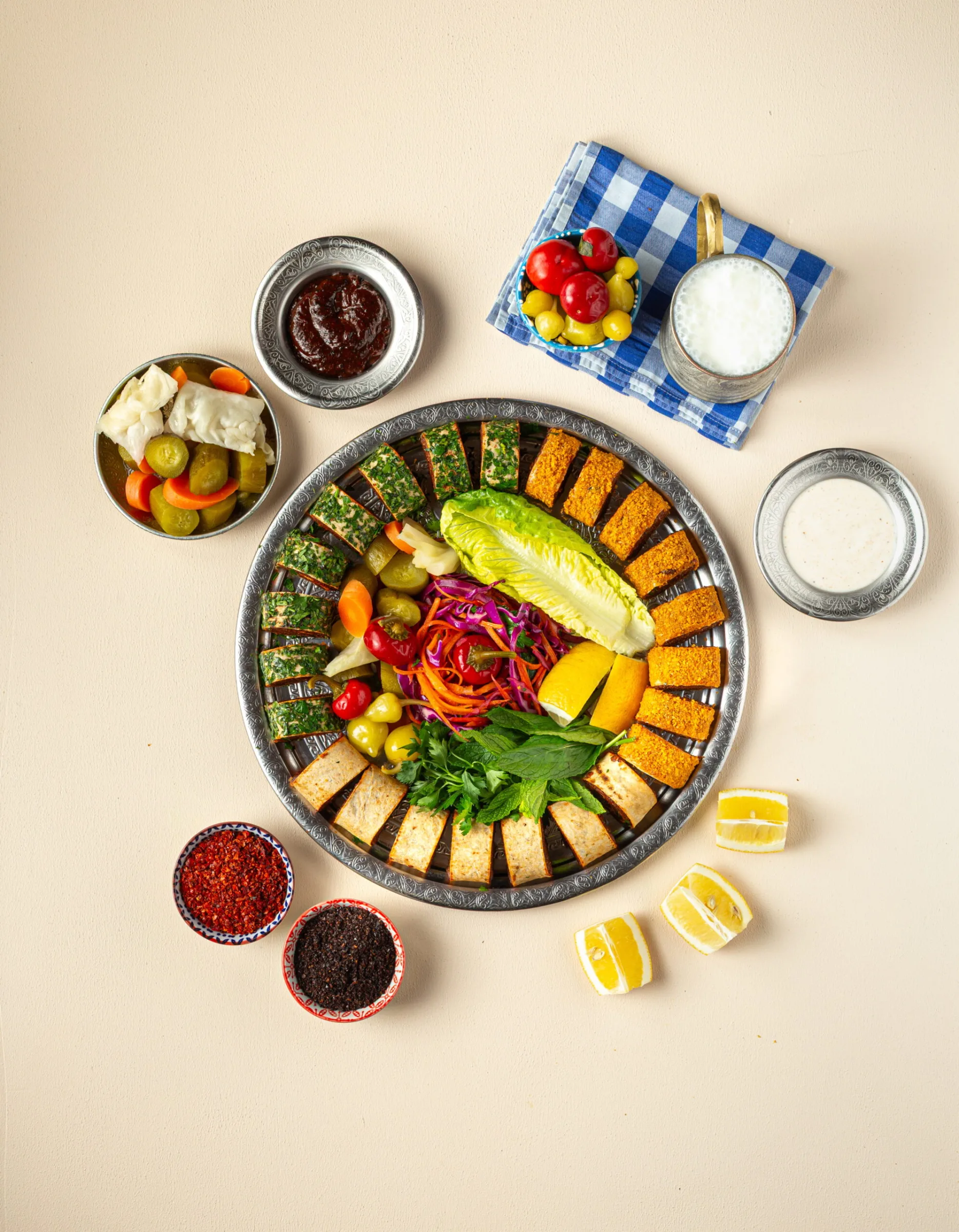 Round platter of çiğ köfte rolls and wraps with lettuce, salad and lemon, surrounded by sauces and pickles