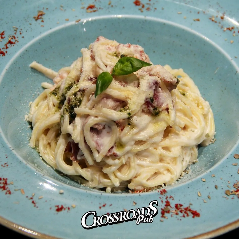 Plate of creamy spaghetti carbonara with mushrooms and fresh basil in a blue bowl