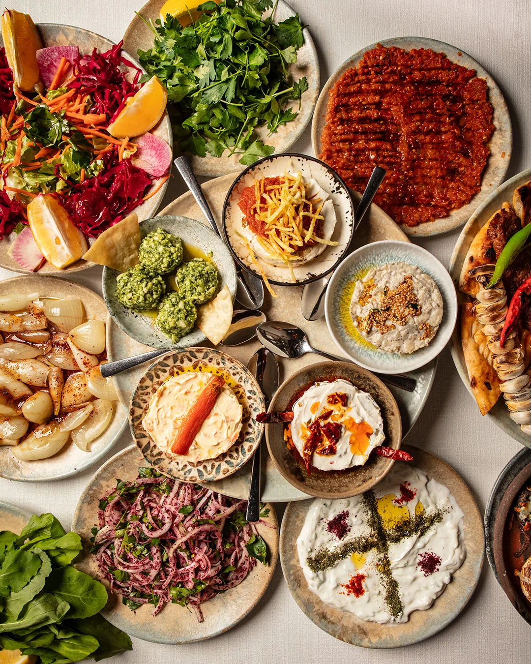 Table covered with small meze plates, salads, ezme, herbs and dips