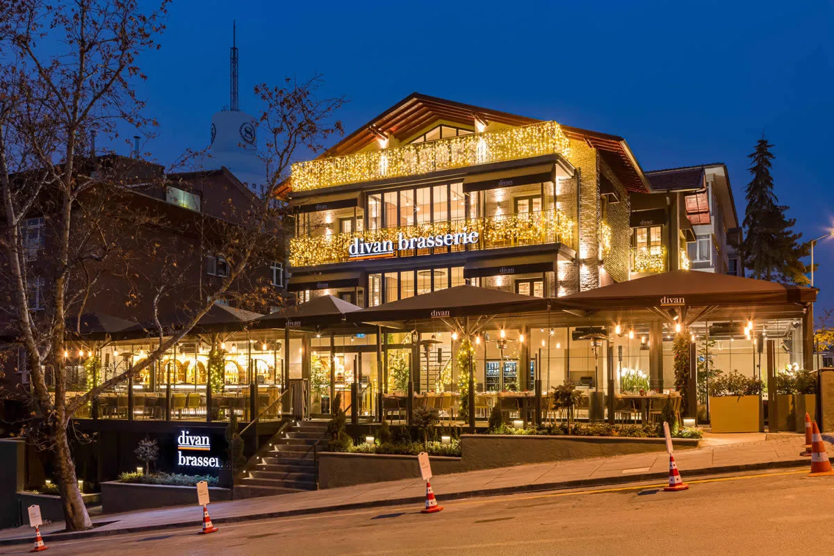 Divan Brasserie Çankaya building lit up at night with a glass-walled terrace at street level